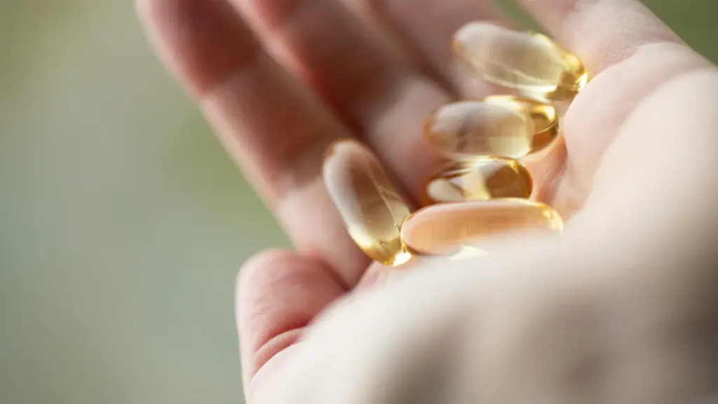 Cilvēka plauksta, kurā atrodas vairākas dzeltenas D vitamīna kapsulas tumšajā sezonā.