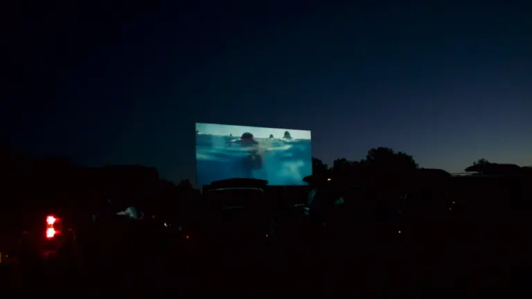 Liela kino ekrāna projekcija brīvā dabā tumšajā diennakts laikā zem debessjuma.