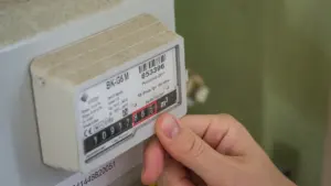 Cilvēks pārbauda elektrības skaitītāja rādījumus ikdienas enerģijas patēriņa uzskaitei mājās.