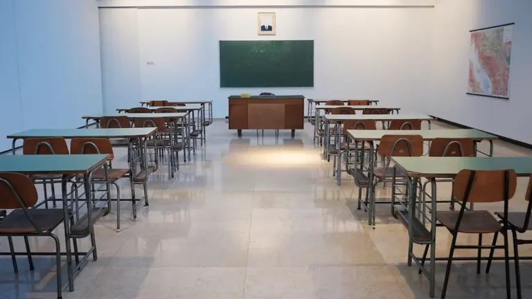 Tukša skolas klase ar soliem un tāfeli, radot nostalģisku un pārdomu pilnu atmosfēru.