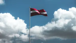 Plazgančiai plevėsuojanti Latvijos valstybės vėliava žydrame danguje su baltais debesimis