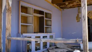 Iekštelpas skats uz pamestu un daļēji sagruvušu dzīvojamo istabu ar plauktiem.